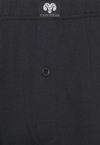 Shorts di cotone blu scuro con chiusura a bottone, dotati di tasca applicata e etichetta logo in vita. Tessuto liscio con cuciture visibili.