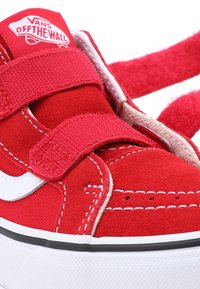 Zapatilla de ante roja con acentos blancos, con correas de Velcro ajustables, detalles de costura y una suela de goma texturizada.