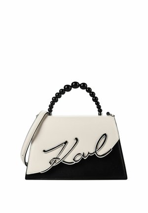 Bolso de mano bicolor en negro y blanco con asa de cuentas y un gran detalle plateado con firma en la parte delantera.