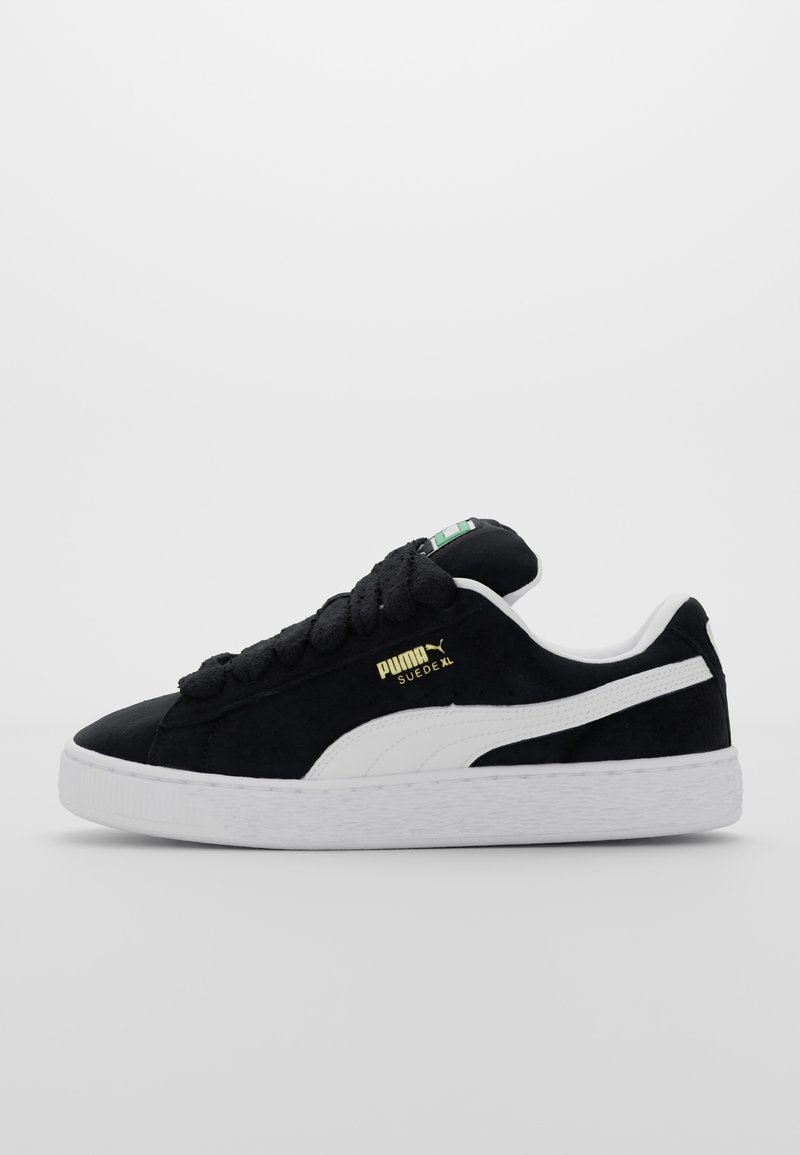 Baskets Puma Suede XL noires avec bande latérale blanche, lacets noirs épais, semelle blanche et logo Puma doré sur le côté.