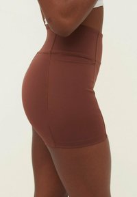 Korkeavyötäröiset, ruskeat urheilushortsit joustavasta materiaalista, joissa on sileä pinta ja minimalistinen muotoilu ilman näkyviä ja merkkejä tai kuvioita.