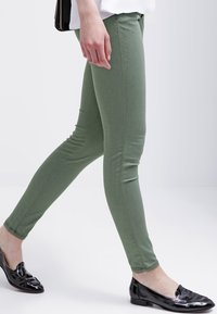 Vihreät kapeat housut joustavaa kangasta, joissa on sileä pinta ja fitted-muotoilu. Yhdistetty kiiltäviin mustiin tasarengashousuihin.