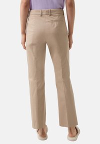 Beige straight-leg pants with belt loops, back pocket, and smooth texture. Worn with light-colored footwear, viewed from the back.