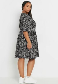 Musta kukkamekko, jossa on valkoisia kukkia, lyhyet puffi-hihat, kapea vyötärö ja polvimittainen hame, yhdistettynä valkoisiin lenkkareihin.