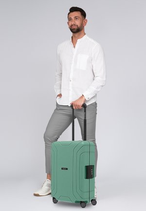 Valigia rigida di colore verde menta con strisce testurizzate, manico retrattile, quattro ruote e lucchetto combinato.