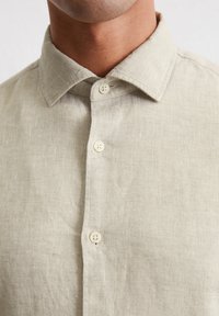 Chemise boutonnée en lin beige clair avec un col classique, dotée de deux boutons sur le devant et d'un tissu lisse et texturé.