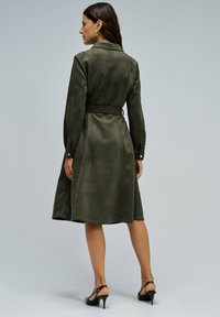 Robe vert olive en suédine avec une taille cintrée, des manches longues et une jupe évasée. Dotée d'un col et de poignets boutonnés.