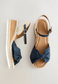 Sandali espadrille blu navy con un fiocco in tessuto, piattaforma in juta intrecciata e soletta in pelle color cuoio, dotati di una cinghia alla caviglia con fibbia dorata.