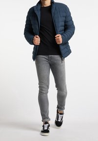 Laivastonsininen puhvijakku, jossa on tikattu muotoilu, vetoketjukiinnitys ja korkea kaulus. Yhdistetty mustan paidan, vaaleanharmaiden farkkujen ja mustien lenkkarien kanssa.