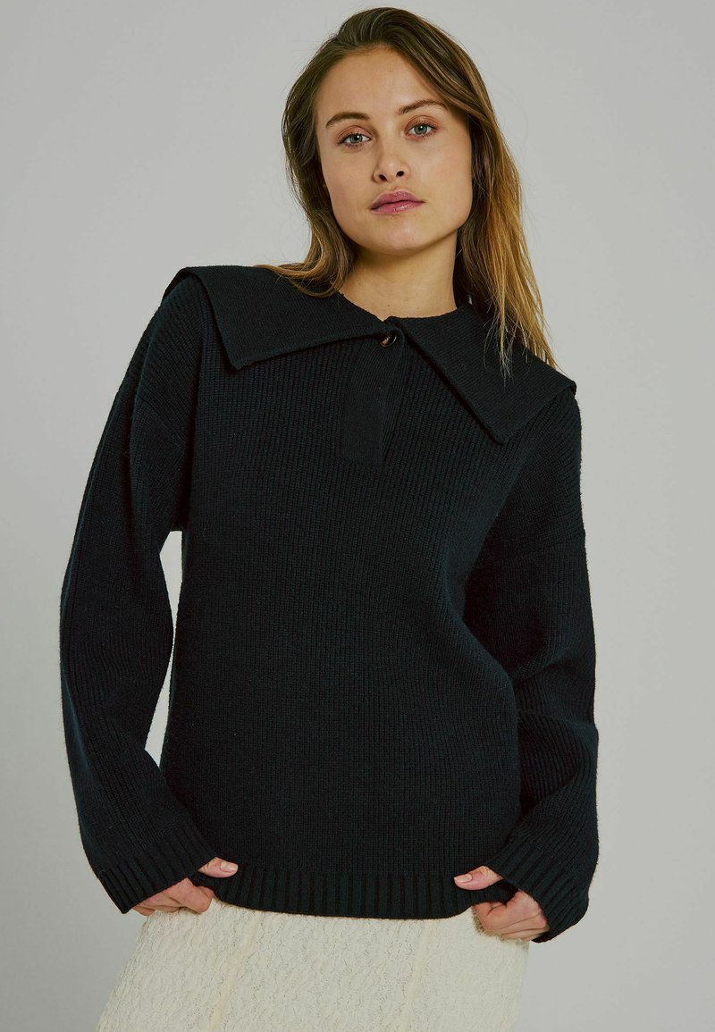 Schwarzer Strickpullover mit weitem Kragen, gerippter Textur und lockerer Passform. Verfügt über einen Knopfverschluss am Hals und lange Ärmel.
