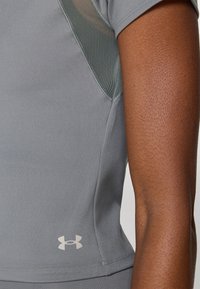 Siva sportska majica kratkih rukava s mrežastim umecima. Under Armour logo u svijetlosivoj boji na rubu, glatka tkanina s laganim rastezanjem.