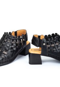 Chaussures noires en cuir à bout ouvert avec un design tissé, dotées d'un petit talon empilé et d'une semelle intérieure beige, accentuées par un petit détail métallique.