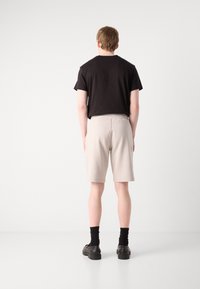 T-shirt noir à manches courtes et shorts beige clair en tissu doux, avec une taille élastique, vus de dos avec des chaussures et des chaussettes noires.