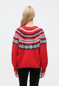 Κόκκινο πλεκτό πουλόβερ με διακοσμητικό άνω μέρος σε λευκό, μαύρο και σκούρο κόκκινο χρώμα. Στρογγυλή λαιμόκοψη και ελαφρώς φαρδιά εφαρμογή. Απαλή υφή.