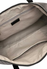 Innenraum einer grauen Stoff-Reisetasche mit einer Reißverschlusstasche und einer flachen Einschubtasche. Verfügt über einen schwarzen Reißverschluss und ein Markenlabel. Glatte Textur, unstrukturiertes Design.