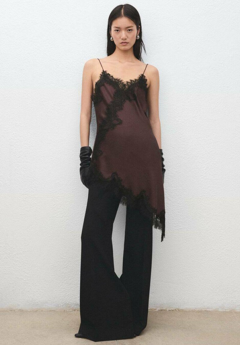 Top de satén marrón con ribete de encaje negro, dobladillo asimétrico y tirantes delgados, combinado con pantalones negros de talle alto y guantes negros.