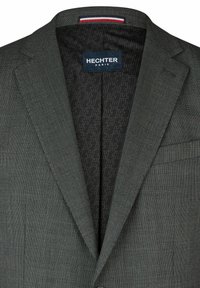 Dunkelgrauer Blazer mit einer strukturierten, gepunkteten Außenseite. Das Innenfutter hat eine schwarze Einfassung mit einem dezente Muster und einem Hechter Paris Etikett.