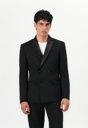 Svart dobbeltradet jakke med sateng lapel, strukturert passform og to sidelommer, kombinert med en hvit t-skjorte med rund hals.