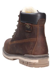 Bota de cuero marrón con un cuello acolchado, ojales de metal y una suela de goma duradera. Detalles notables incluyen costuras y un logotipo en el lateral.