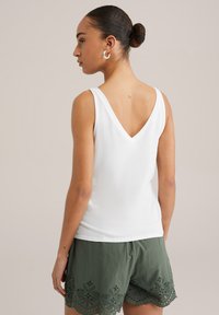 White sleeveless top with a V-neck, paired with olive green shorts featuring a patterned hem. Soft fabric with a smooth texture.