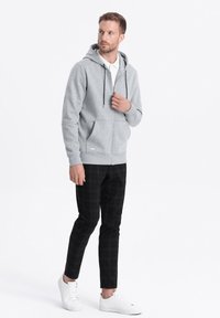 Haut à capuche zippé gris avec cordon de serrage, poches avant et poignets côtelés, associé à un pantalon slim à carreaux noirs et des baskets blanches.