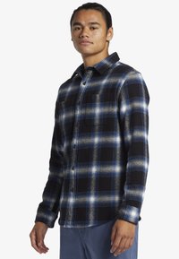 Schwarz-blau kariertes Flanellhemd mit hellblauen und weißen Akzenten, zwei Brusttaschen, knopfbares Design und Kragen.