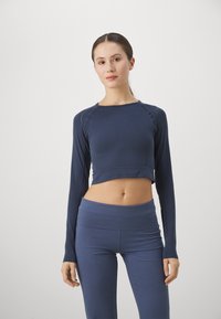 Sötétkék, hosszú ujjú, cropped top bordás textúrával és díszítő varrásokkal, melyet illő, magas derekú leggingsszel párosítottak.