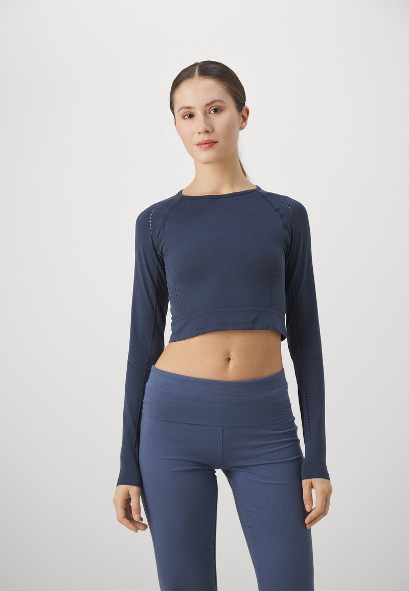 Sötétkék, hosszú ujjú, cropped top bordás textúrával és díszítő varrásokkal, melyet illő, magas derekú leggingsszel párosítottak.