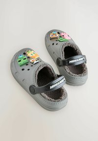 Sabots gris avec doublure en peluche, dotés d'une bride noire avec le logo "Minecraft" et des détails colorés de personnages sur le dessus.