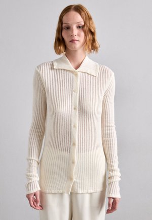 Helle elfenbeinfarbene Rippstrickjacke mit weitem Kragen, langen Ärmeln und Knopfverschluss. Hergestellt aus weichem, strukturiertem Stoff mit vertikalen Streifen.
