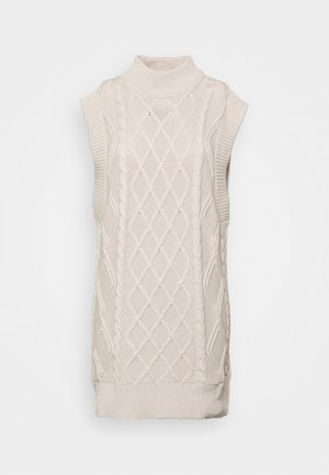 Robe-pull sans manches crème en maille avec col montant et motifs torsadés et losanges, présentée sur un fond uni.