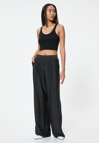 Zwarte geribbelde crop top en wijde broek met witte verticale strepen en stippen. De broek heeft een gemêleerde tailleband en zakken.