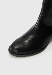 Black ankle boot made of textured material resembling snake skin, featuring a pointed toe and a smooth, shiny finish.