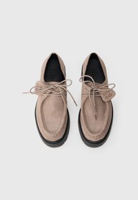 Chaussures en suede beige à lacets avec un bout rond, semelle en caoutchouc noire contrastante et une petite étiquette affichant le nom de la marque "HUGO."