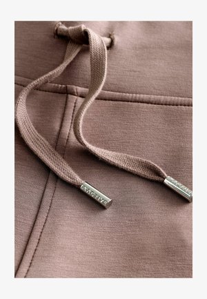 Bluza w kolorze pudrowego różu z plecionymi sznurkami. Srebrne metalowe końcówki z logo. Miękka tekstura i gładka powierzchnia materiału.