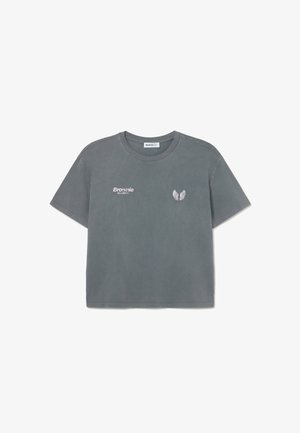 Camiseta gris de manga corta con cuello redondo, texto "Brownie No Limits" en el pecho izquierdo y pequeño emblema con alas en el pecho derecho.