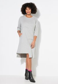 Robe grise longueur genoux avec des manches 3/4, un col rond et des poches latérales. Présente un ourlet légèrement asymétrique et un tissu texturé. Bottines noires avec clous.