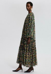 Blomstrede maxikjole med lange ærmer, lagdelte lag, sort baggrund og farverige blomster. Kombinationen med sorte hælhæle slingback-sko.