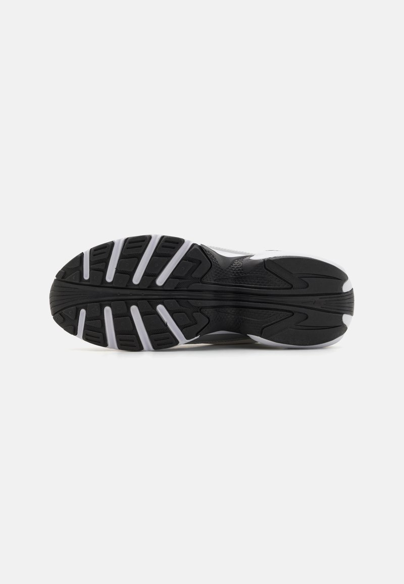Suela de zapato deportivo negro con una superficie de goma texturizada, patrones de banda de rodadura distintos y acentos blancos a lo largo de los bordes.