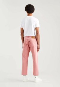 Jean en denim rose avec une coupe droite, doté d'un patch en cuir marron à l'arrière de la taille. Assorti à un t-shirt blanc uni et des baskets blanches.