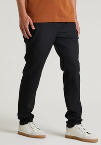 Svarta träningsbyxor med en slät textur, insvängd design och elastisk midja, matchade med vita sneakers med gummisulor.