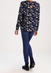 Blusa floreale blu navy con maniche lunghe, dotata di un dettaglio a chiave sul retro, abbinata a jeans skinny blu scuro e stivali ankle neri.
