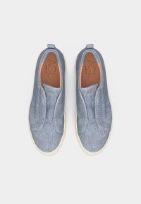 Ζεύγος μπλε τζιν αθλητικών παπουτσιών τύπου slip-on με λευκές σόλες και λογότυπο AGL στη γλώσσα, εμφανιζόμενα από πάνω σε λευκό φόντο.