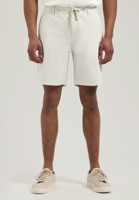 Helle beige Baumwollshorts mit einem elastischen Kordelzugbund, seitlichen Taschen und einer lockeren Passform, kombiniert mit sneakers in neutralen Farben.