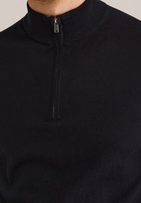 Maglione nero con zip sul collo realizzato in tessuto morbido. Presenta un colletto a costine e una leggera lucentezza, con una zip di un quarto di lunghezza per un'apertura del collo regolabile.
