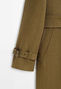 Manche de manteau en tissu marron texturé avec sangle ajustable et détail de boucle rectangulaire noire.