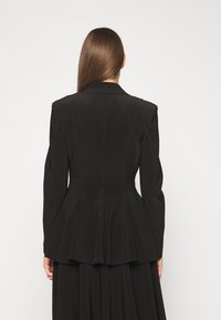 Černá peplum bunda s vysoce kvalitním střihem, strukturovanými rameny a dlouhými rukávy. Obsahuje viditelné švy a hladkou texturu.