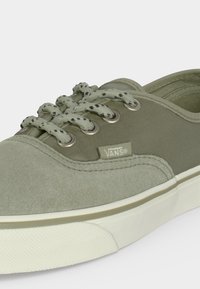 Ανοιχτοπράσινο αθλητικό παπούτσι Vans με λευκή σόλα, κορδόνια με σχέδια και ορατό λογότυπο Vans στη πλευρά κοντά σε μεταλλικές ρινικόλες.