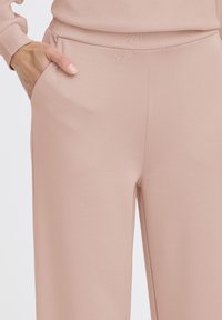 Hellrosa Jogginghose mit glatter Textur, elastischem Bund, Seitentaschen und einem lockeren Schnitt, geeignet für die Freizeitkleidung.