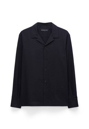 Chemise noire à manches longues avec boutons, en tissu texturé et col pointu, posée à plat sur un fond blanc.